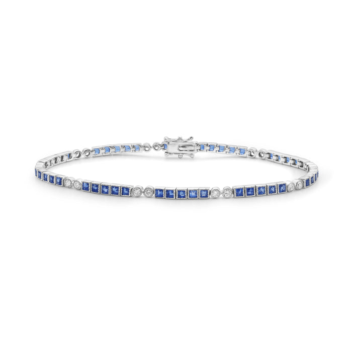 A 14K white gold tennis bracelet with blue sapphires and diamonds, featuring a clasp and a safety mechanism.