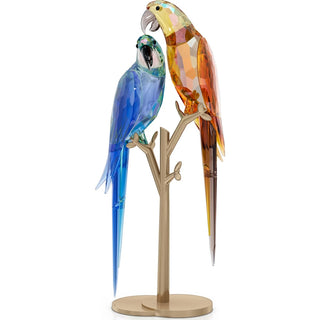 Two colorful parrot figurines on a branch stand against a white background