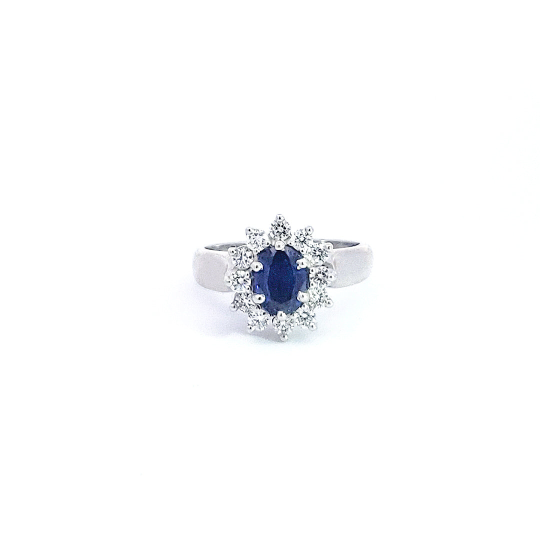 Ring with a blue gemstone and diamond halo on a white background