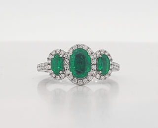 Ring with three emerald stones and diamond-studded band on a white background